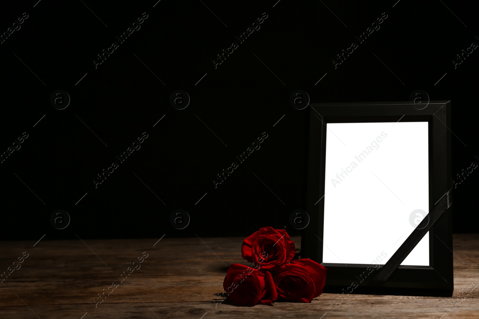 Photo of Empty frame with black ribbon and roses on table. Funeral symbol