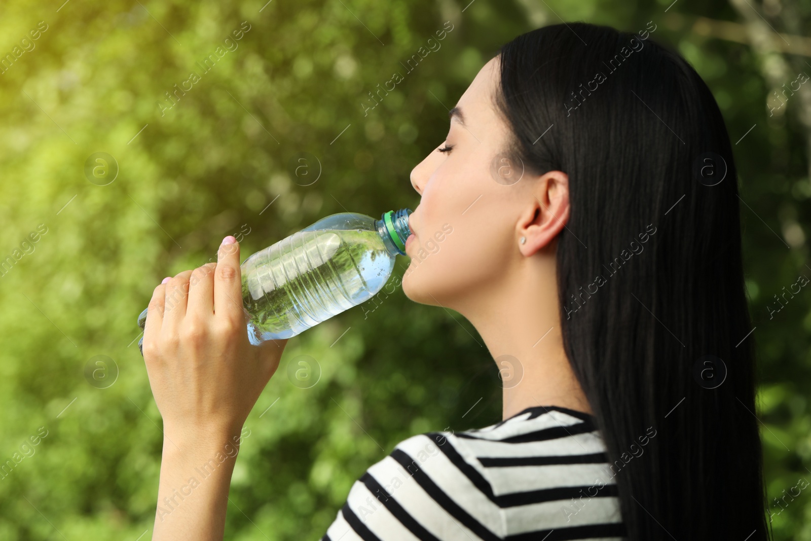 Photo of Beautiful young woman drinking water outdoors. Refreshing drink