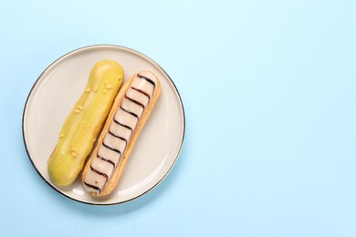 Photo of Delicious eclairs covered with glaze on light blue background, top view. Space for text