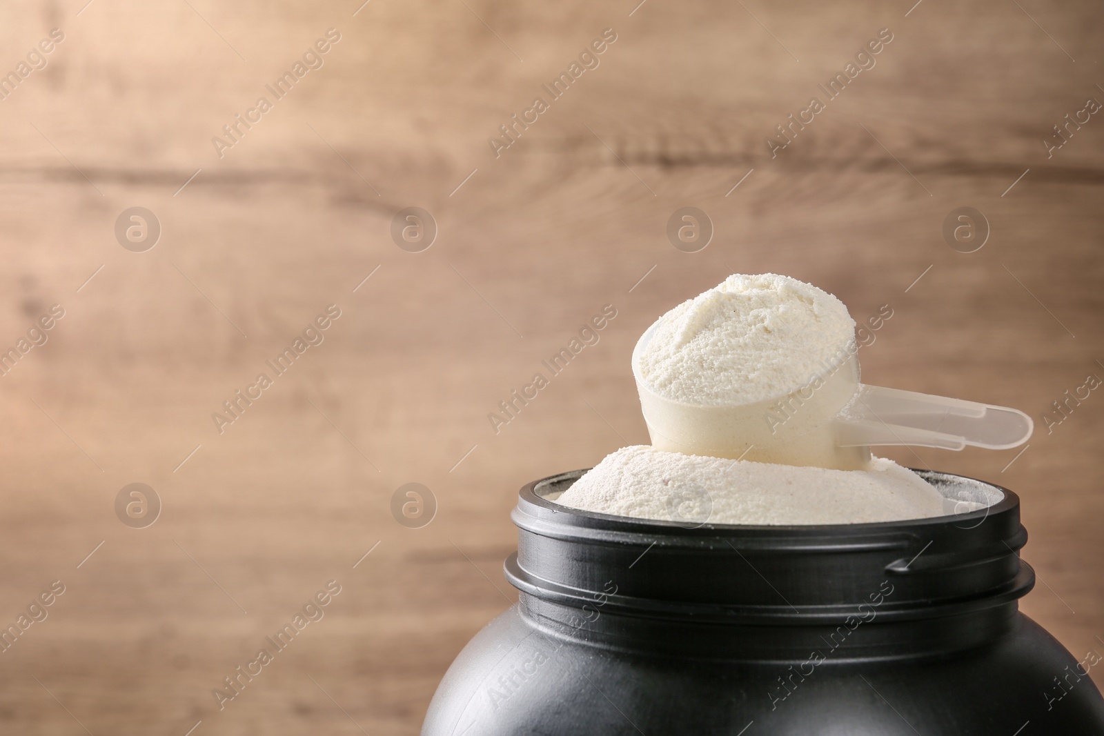 Photo of Black jar with measuring scoop of protein powder against wooden background. Space for text