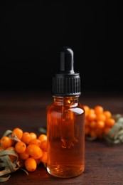 Ripe sea buckthorn and bottle of essential oil on wooden table against black background