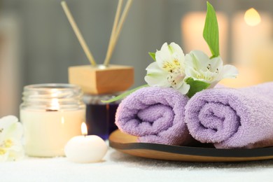 Beautiful composition with different spa products and flowers on white towel against blurred background, closeup