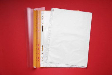 Photo of File folder with punched pockets and paper sheets on red background, flat lay. Space for text