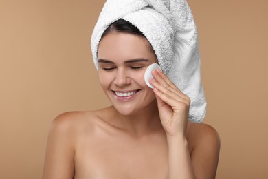 Photo of Young woman cleaning her face with cotton pad on beige background