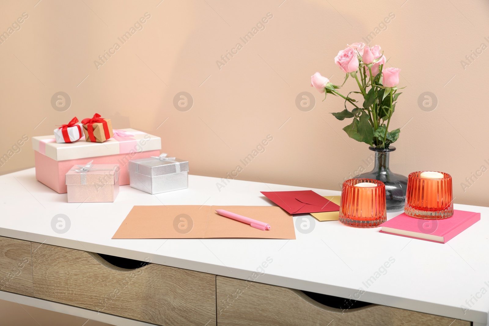 Photo of Greeting card, flowers and candles on white table indoors