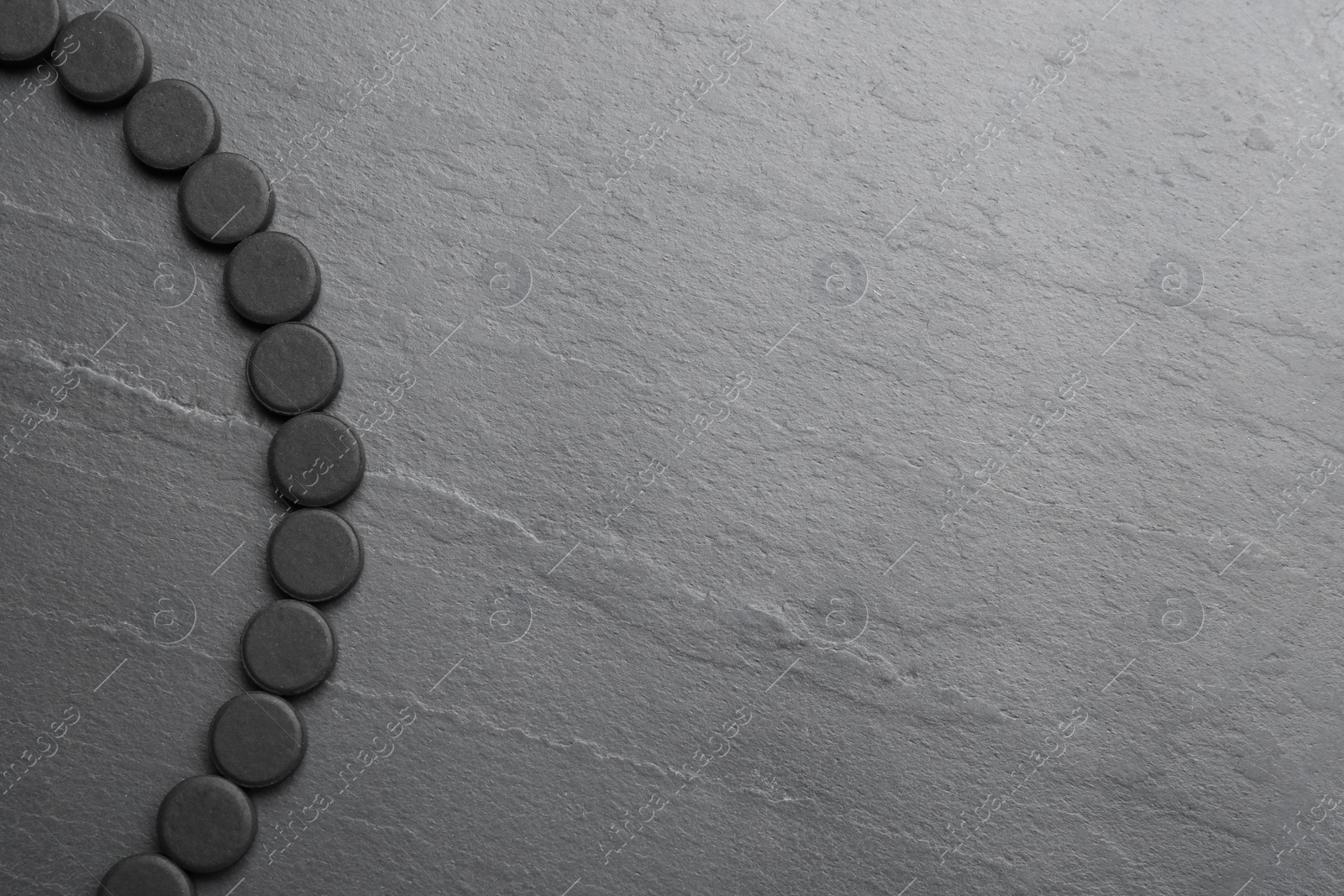 Photo of Activated charcoal pills on black table, flat lay with space for text. Potent sorbent
