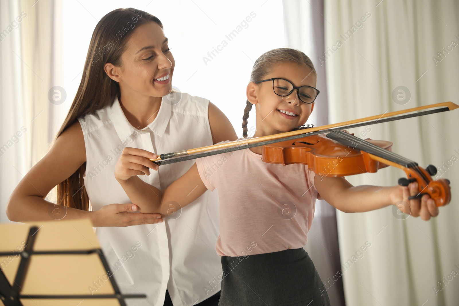 Photo of Young woman teaching little girl to play violin indoors