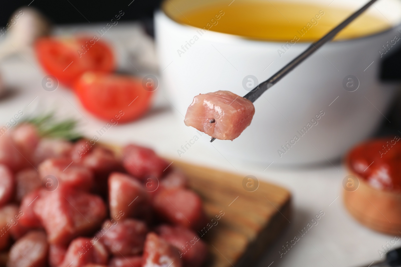 Photo of Fork with raw meat and blurred fondue pot on background, closeup