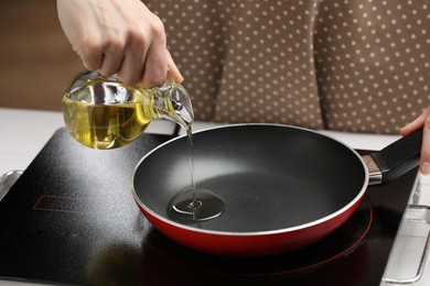 Photo of Vegetable fats. Woman pouring cooking oil into frying pan on stove, closeup