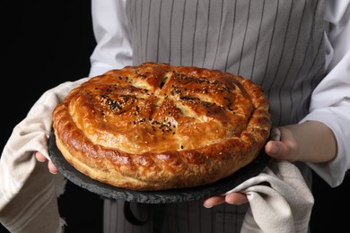 Photo of Woman holding tasty homemade pie on black background, closeup