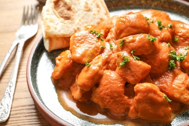 Photo of Plate of delicious butter chicken on wooden table, closeup. Traditional Murgh Makhani dish