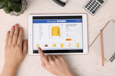 Woman with tablet shopping online at white wooden table, top view