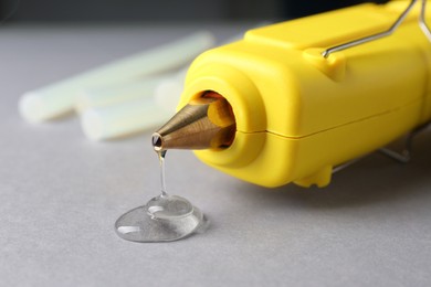 Photo of Melted glue dripping out of hot gun nozzle on grey background, closeup