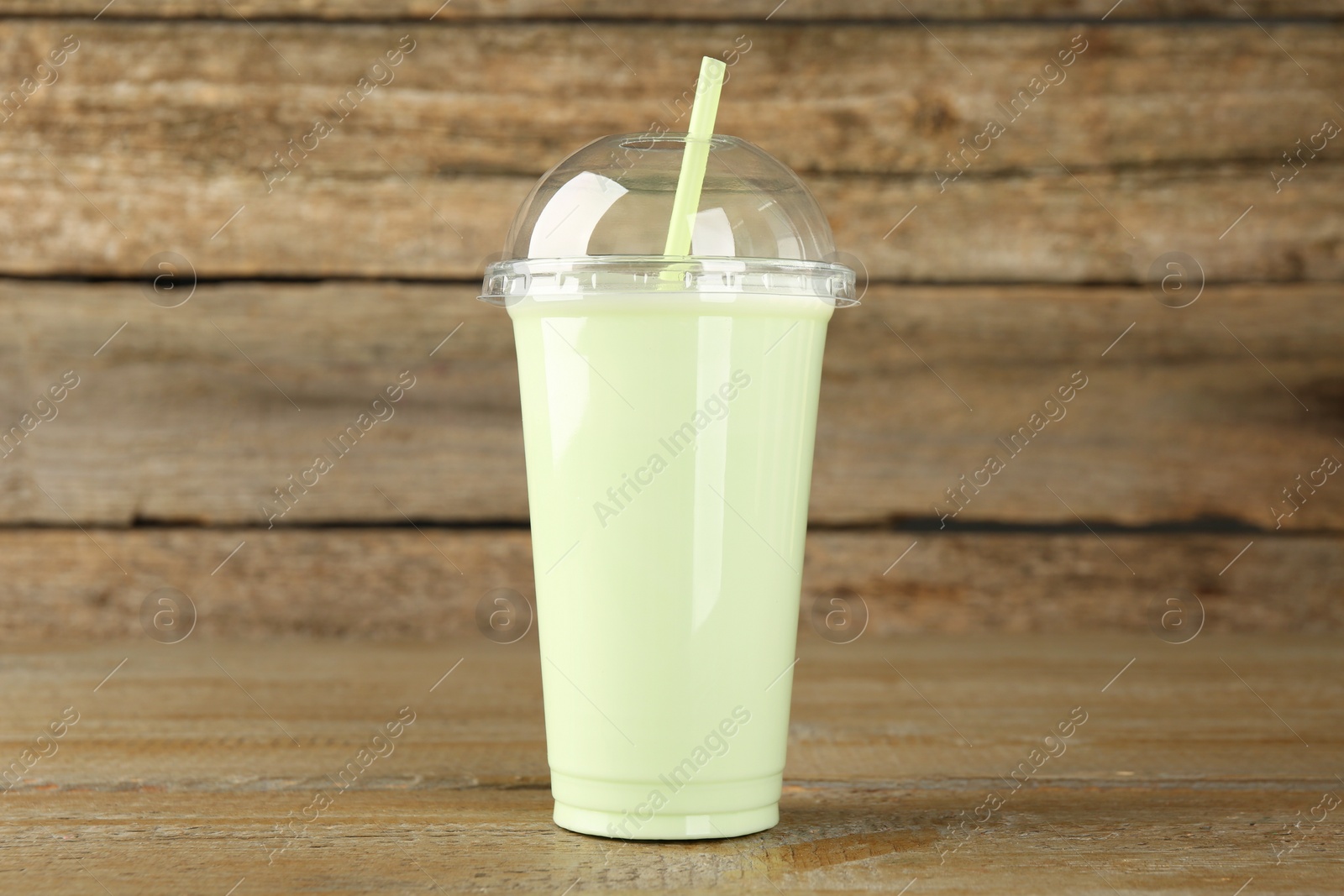 Photo of Plastic cup of tasty smoothie on wooden table