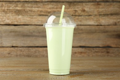 Photo of Plastic cup of tasty smoothie on wooden table