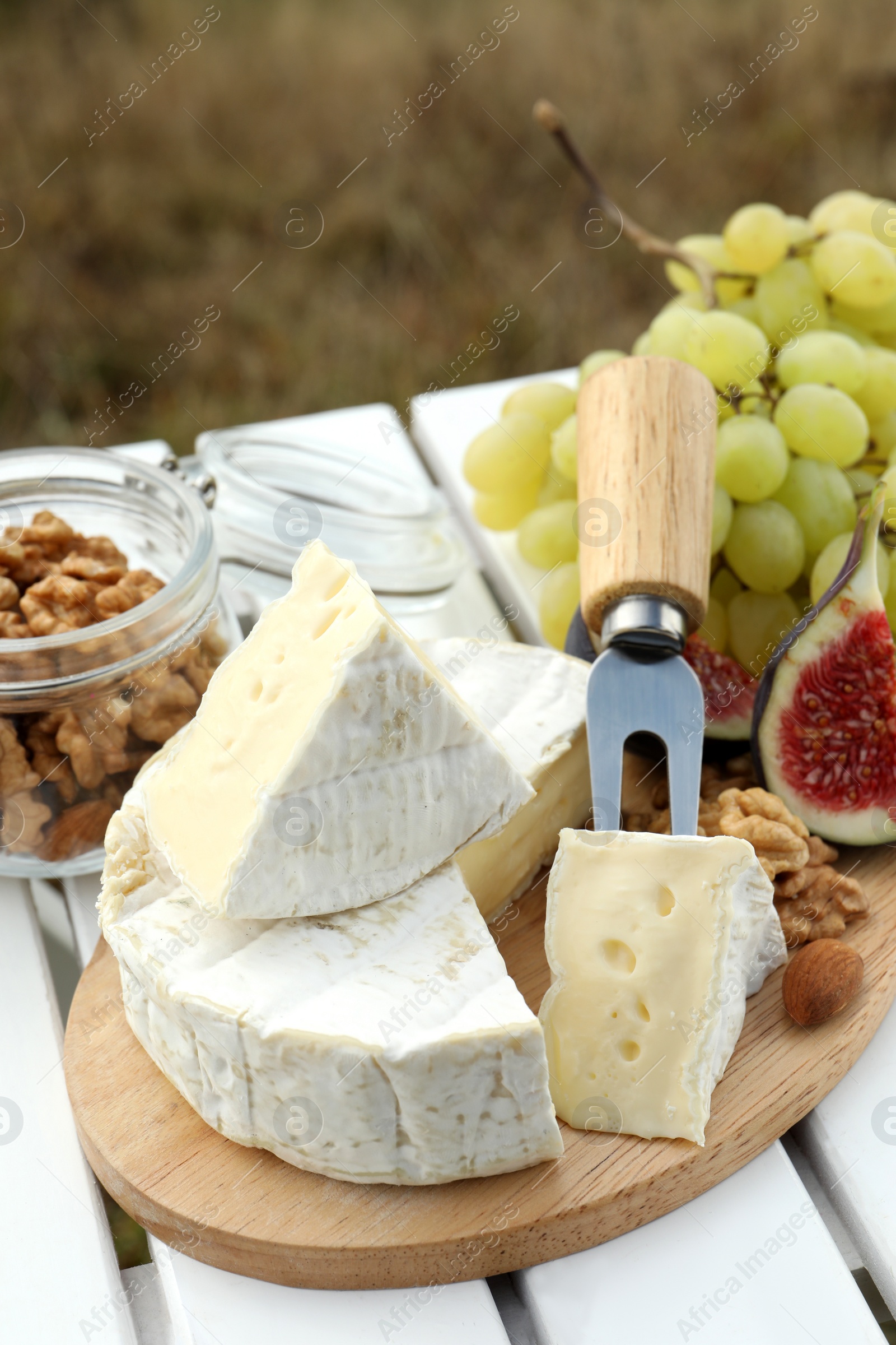 Photo of Delicious cheese, nuts and fruits on white wooden table outdoors
