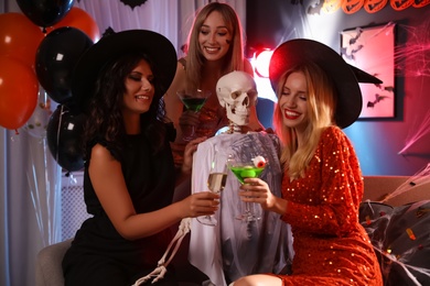 Women with cocktails near skeleton at Halloween party