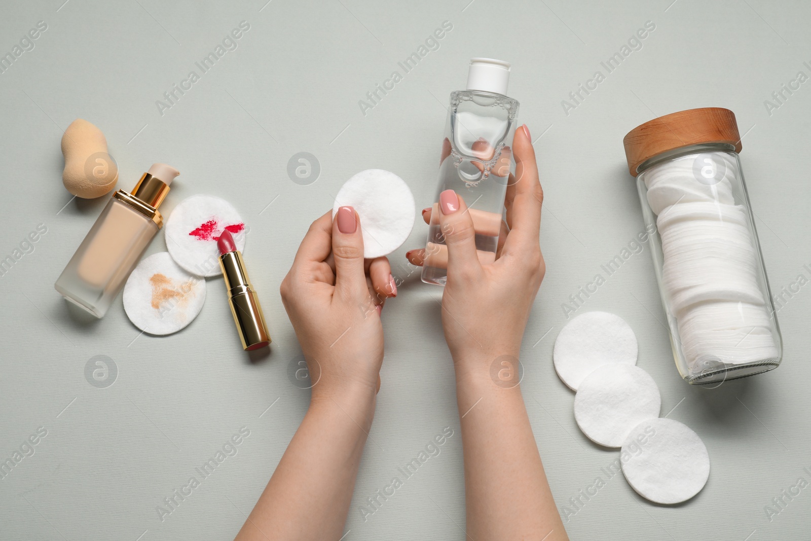 Photo of Woman with makeup remover, cotton pads, lipstick, foundation and sponge on light grey background, top view