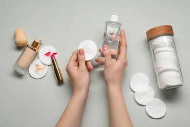 Woman with makeup remover, cotton pads, lipstick, foundation and sponge on light grey background, top view