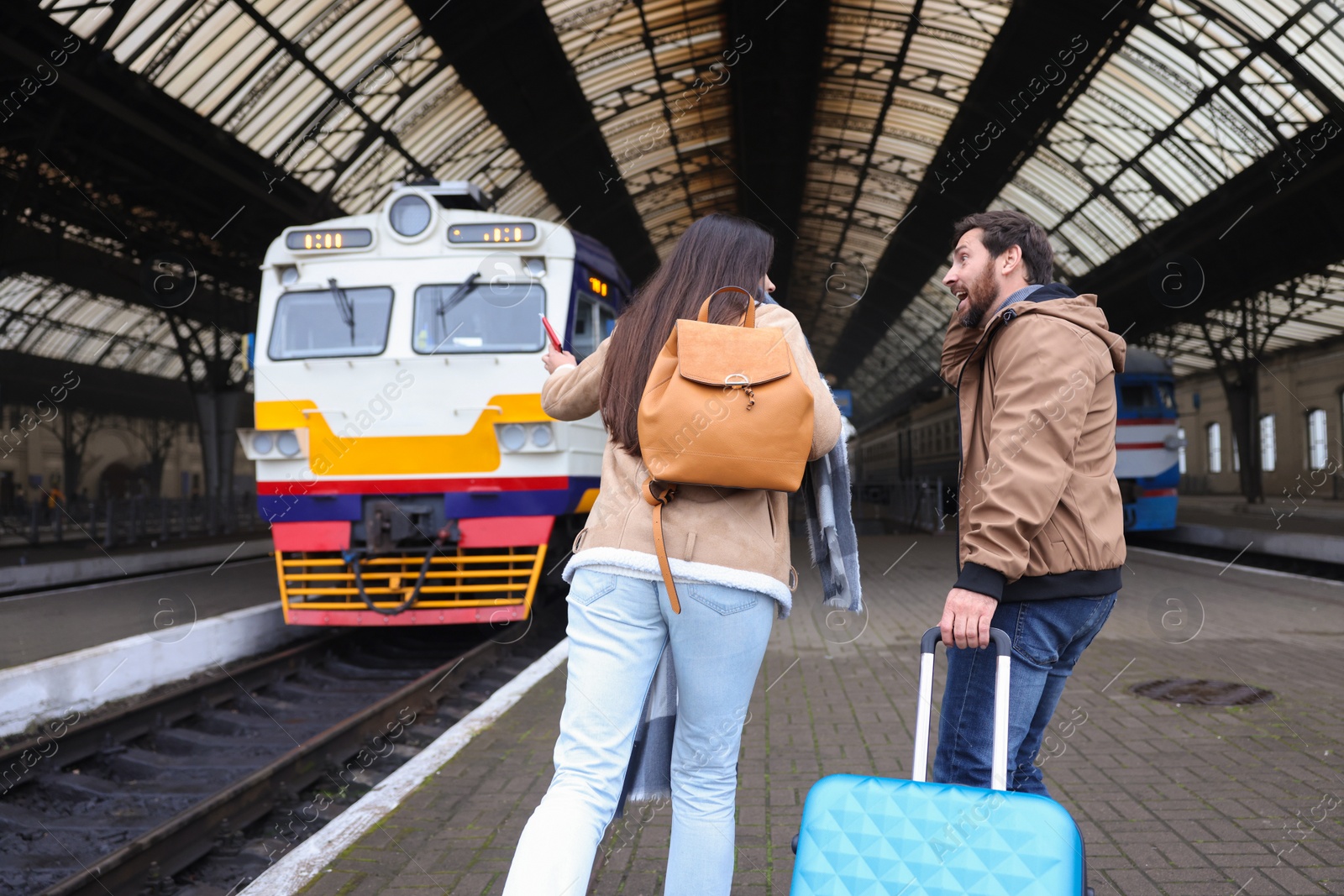 Photo of Being late. Couple with suitcase running towards train at station, back view