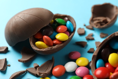 Photo of Broken chocolate eggs with candies on light blue background, closeup