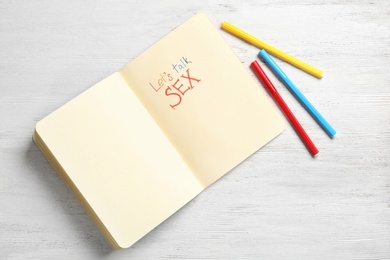 Photo of Notebook with phrase "LET'S TALK SEX" on white wooden background, flat lay. Space for text