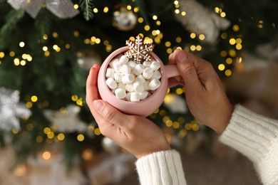 Photo of Woman holding cup of delicious Christmas cocoa with marshmallows and gingerbread against blurred lights, above view