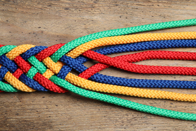 Photo of Braided colorful ropes on wooden background, top view. Unity concept