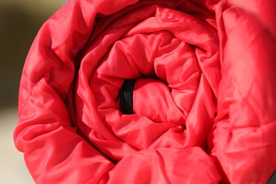 Photo of Red sleeping bag on blurred background, closeup. Camping equipment