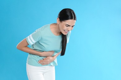 Photo of Woman suffering from stomach ache on light blue background, space for text. Food poisoning