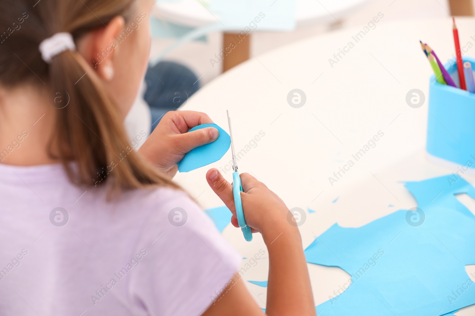Photo of Little girl cutting color paper with scissors at desk, closeup. Kindergarten activities
