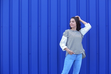 Photo of Young hipster woman in stylish jeans posing near color wall