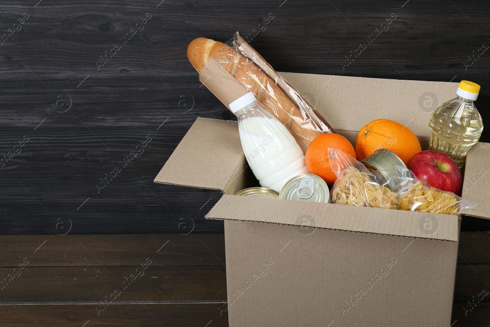 Photo of Cardboard box with donation food on wooden table, closeup. Space for text