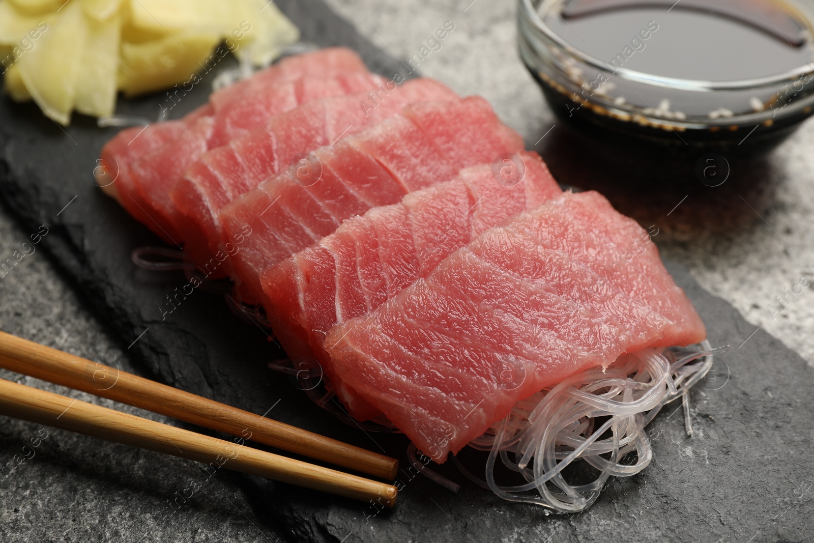 Photo of Tasty sashimi (pieces of fresh raw tuna), glass noodles and chopsticks on black board, closeup