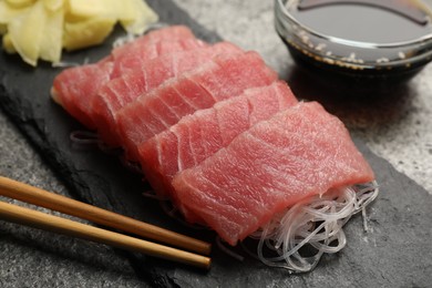 Photo of Tasty sashimi (pieces of fresh raw tuna), glass noodles and chopsticks on black board, closeup