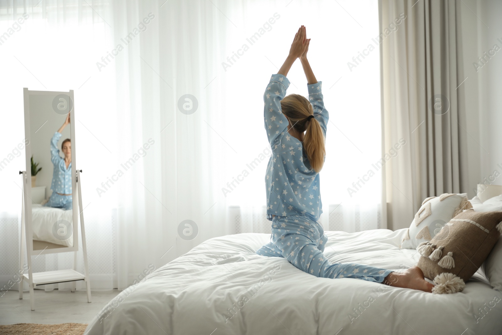Photo of Young woman doing gymnastics on bed at home. Morning fitness
