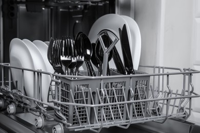 Photo of Open modern dishwasher with clean tableware, closeup