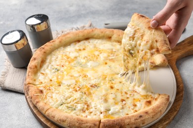 Woman taking piece of delicious cheese pizza at light grey table, closeup