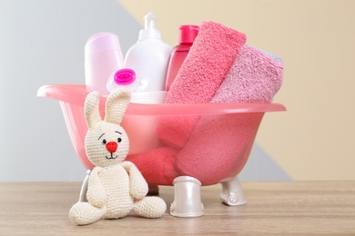 Baby cosmetic products, knitted rabbit and towels on table against color background