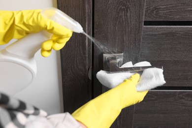 Photo of Woman cleaning door handle with detergent and rag indoors, closeup