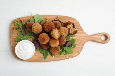 Delicious falafel balls with herbs and sauce on white wooden table, top view