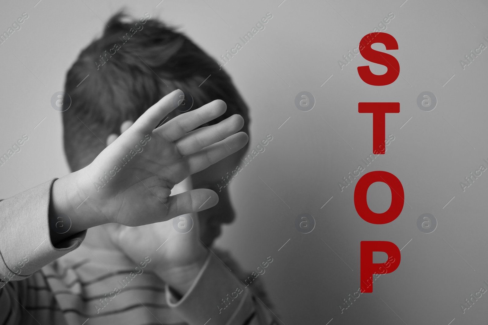 Image of No child abuse. Boy making stop gesture near grey wall, selective focus. Black and white effect