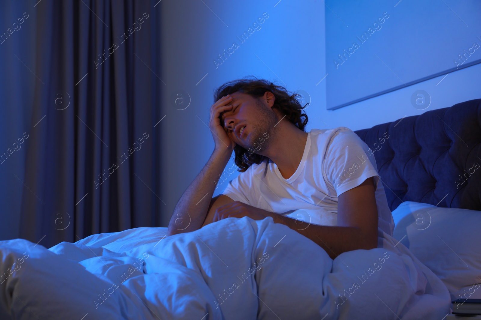 Photo of Handsome young man suffering from insomnia in dark room at night. Bedtime