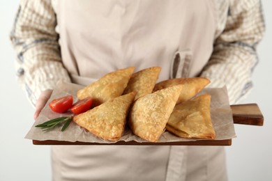 Photo of Woman holding wooden board with delicious samosas on white background, closeup