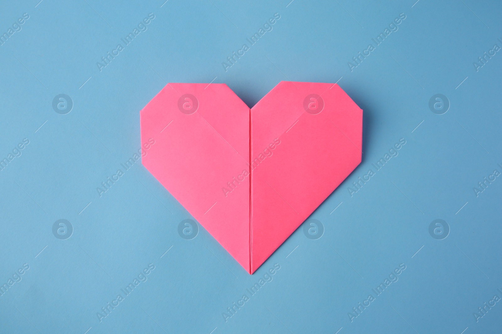 Photo of Origami art. Handmade pink paper heart on light blue background, top view