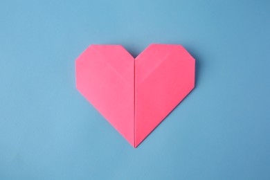 Photo of Origami art. Handmade pink paper heart on light blue background, top view