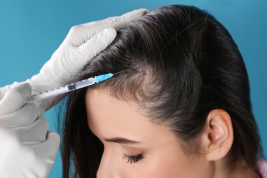 Young woman with hair loss problem receiving injection on color background, closeup