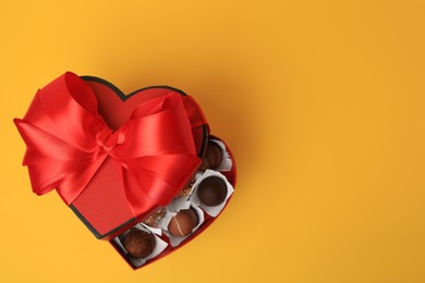 Photo of Heart shaped box with delicious chocolate candies on yellow background, top view. Space for text