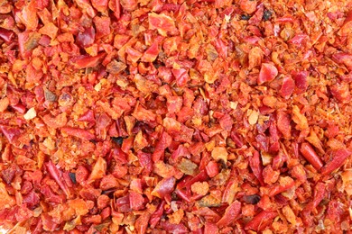 Photo of Aromatic spice. Red chili pepper flakes as background, top view