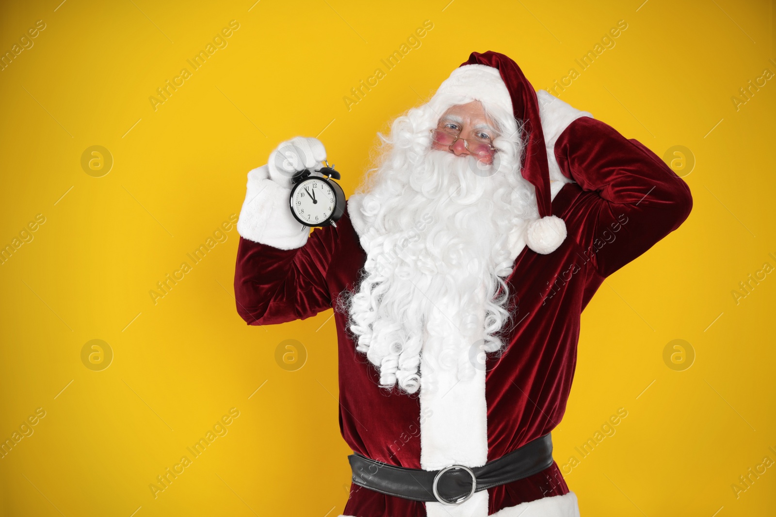 Photo of Santa Claus holding alarm clock on yellow background, space for text. Christmas countdown